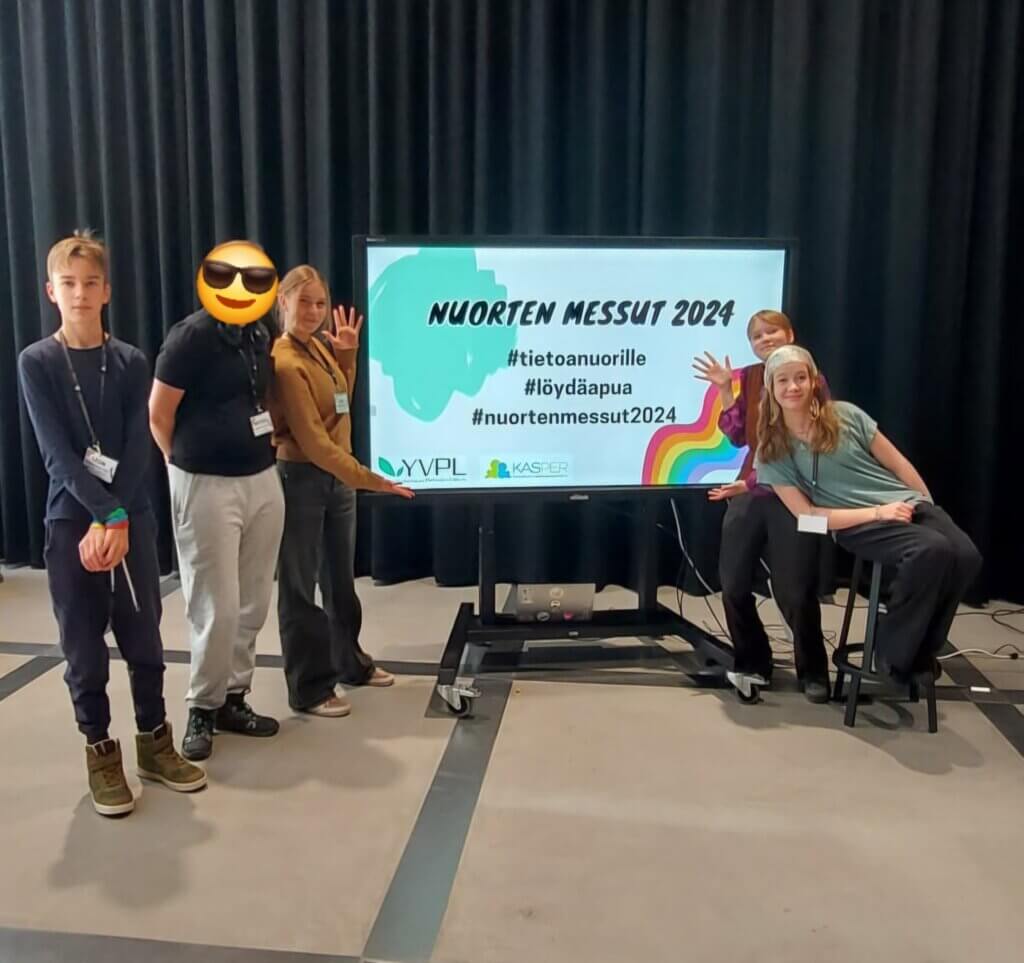 Neljä nuorta poseeraa suuren näytön edessä, jossa lukee Nuorten messut 2024 ja hashtagit #tietoanuorille, #löydäapua, #nuortenmessut2024. Näytön alareunassa on YVPL ja KASPER -logot. Y