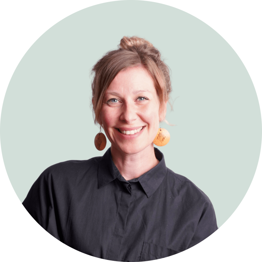 Nainen hymyilee kameralle. Hänellä on yllään musta paita ja puiset korvakorut. Tausta on vaaleanvihreä.