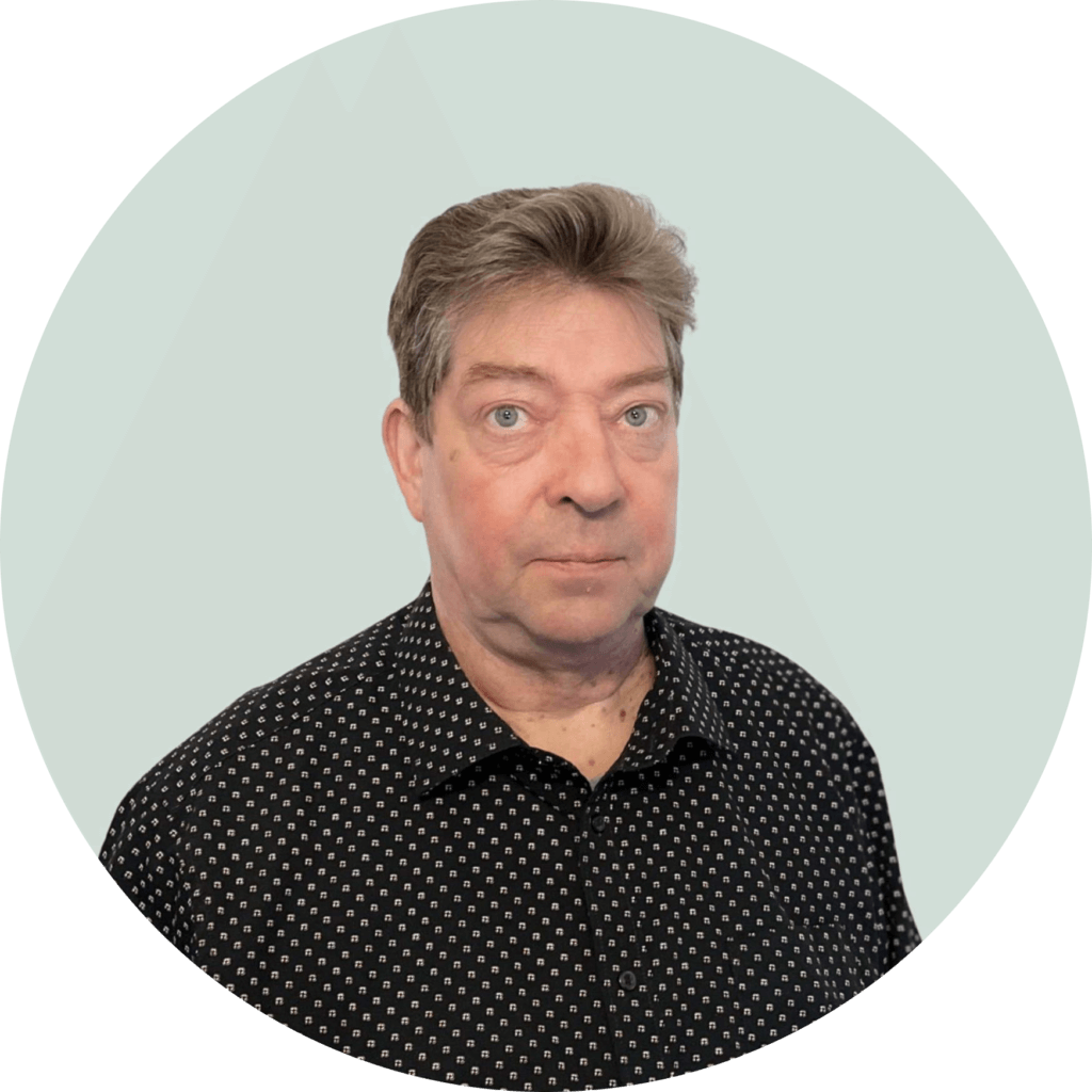 Tämä on kuva henkilöstä, joka seisoo vaalean taustaa vasten. Hänellä on musta kauluspaita, jossa on valkoisia kuvioita. Hän katsoo suoraan kameraan.