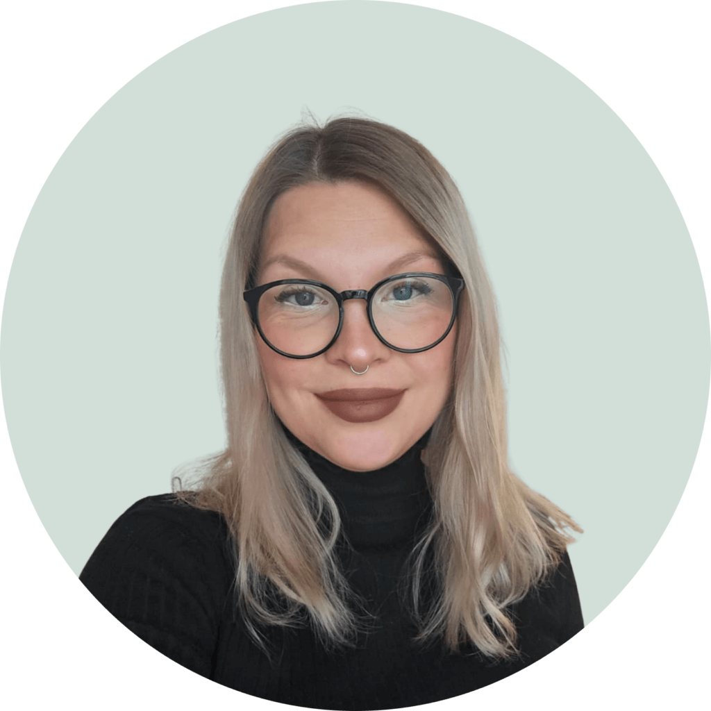 En pysty kertomaan, kuka henkilö kuvassa on, mutta voin kuvata sen. Kuvassa on henkilö, jolla on vaaleat hiukset, mustat silmälasit ja tummanruskea huulipuna. Tausta on vaalean harmaa ja henkilö käyttää mustaa neuletta.