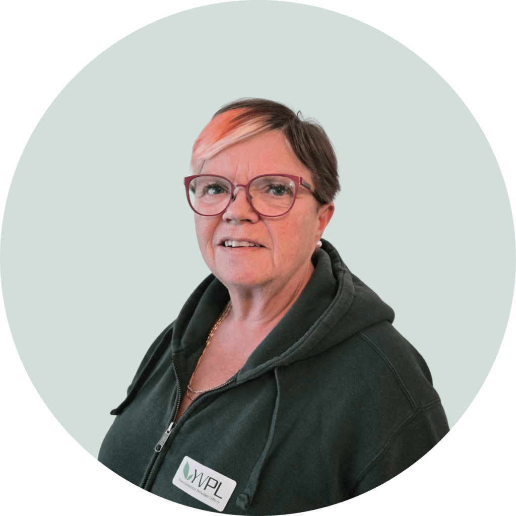 Nainen, jolla on lyhyet hiukset ja silmälasit, pukeutuneena vihreään huppariin, jossa on WVIP-tarra. Hän seisoo vaalean harmaan taustan edessä.