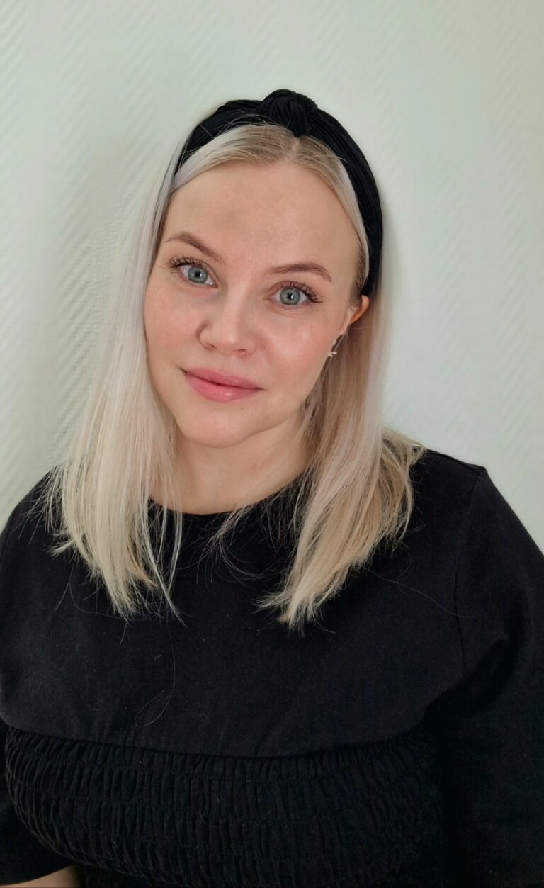 Vaaleahiuksinen nainen katsoo kameraan ja hänellä on musta pääpanta.